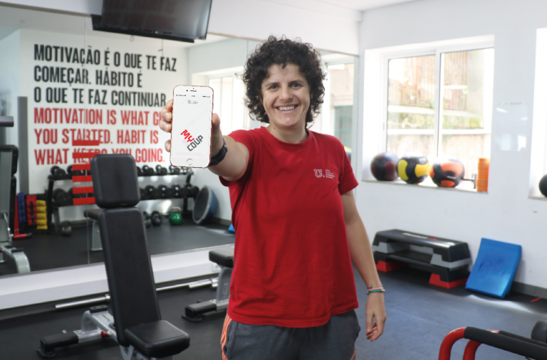 Instrutora de fitness a segurar o telemóvel com a aplicação na sala de musculação do Programa UPFit
