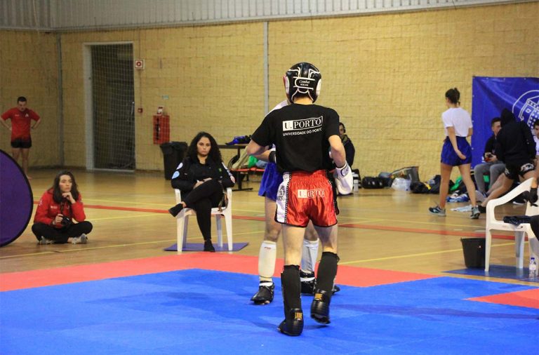 homem com camisola preta da universidade do porto, calções vermelhos e luvas de kickboxing a preparar-se para começar a lutar contra adversário.